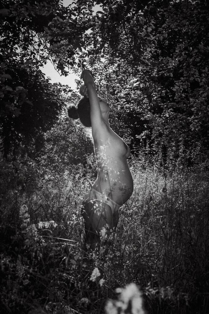 Soul Photo einer schwangeren Frau in Unterhose seitlich in einer Wiese mit hohem Gras.