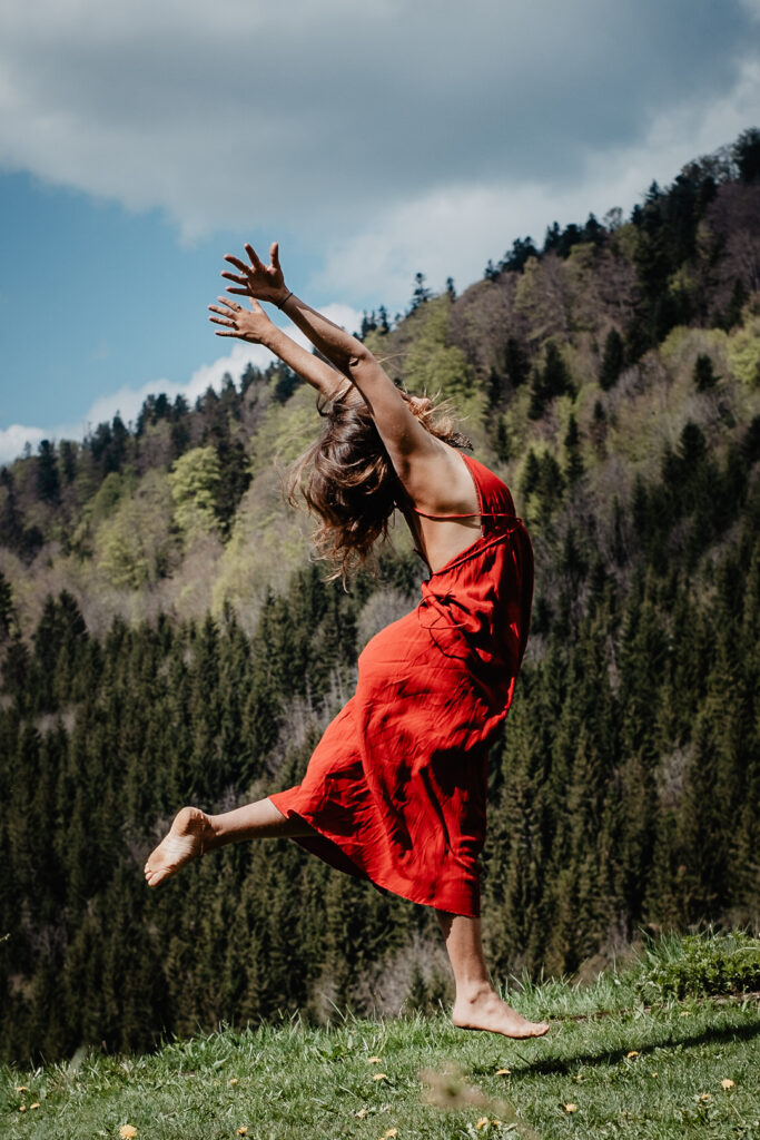 Business Photography während eines wilden Business Shootings in der Natur, bei dem eine Frau in einem roten Kleid springt und von Seelenfotografin begleitet wird.